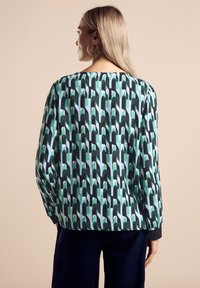 Långärmad blus med ett abstrakt mönster i grön, svart och ljusblått. Slät tyg med en vid halsringning och avslappnad passform.