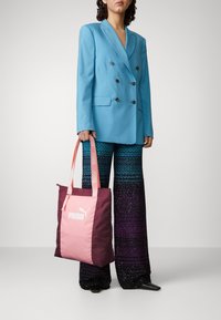 Bolso tote con una mezcla de tela rosa y marrón, que presenta un gran logo de Puma. Asas gruesas con marca en un color rosa más claro.