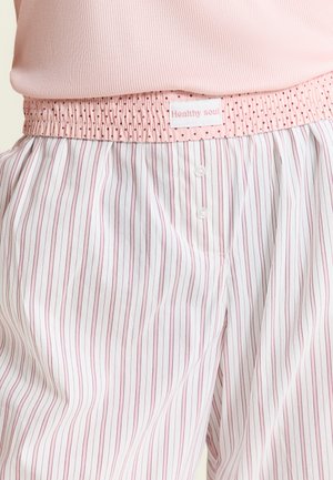 Pantalones de pijama con cinturilla elástica con lunares rosas, tela blanca con finas rayas verticales rosas, combinados con un top rosa acanalado.