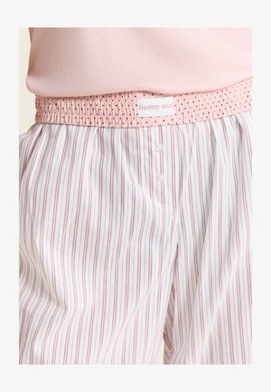 Pyjamahose mit elastischem Bund und rosa Punkten, weißer Stoff mit dünnen vertikalen rosa Streifen, kombiniert mit einem rosa gerippten Oberteil.