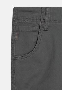 Jeans gris avec une texture lisse, présentant une poche avant et des coutures détaillées le long des seams. Étiquette de marque subtile sur la poche.