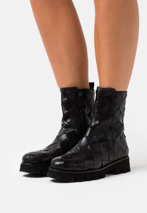 Black leather ankle boots with woven pattern, side zipper, and chunky rubber sole. Features a textured finish and mid-calf height.