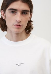 Fehér pamut rövid ujjú póló, amelyen a mellrészen egy kis fekete "Marc O’Polo DENIM" logó található. Simának érződő anyag, laza fazon.
