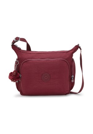 Maroon crossbody bag with front zipper pocket, adjustable strap, side zip pocket, and plush monkey keychain attached to left side.