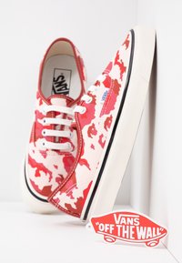 Baskets en toile à camouflage rouge et blanc avec lacets blancs, bordure de semelle noire, et étiquette logo Vans "Off the Wall". Conception à bout arrondi.