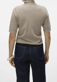 Krémový krátký rukáv turtleneck svetr vyrobený z měkké tkaniny, v kombinaci s tmavě modrými džínami s vysokým pasem, které mají zadní kapsy a viditelné švy.