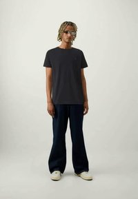 Mørkegrå bomulds t-shirt parret med løse navy denim bukser og hvide sneakers. Accessories inkluderer firkantede solbriller.