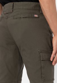 Dark olive green cargo pants feature a sturdy cotton blend material, multiple side pockets, and a small logo patch on the waistband.