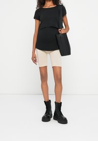 Svart kortärmad topp med lagerdesign, beige cykelshorts och svarta snörkängor. Modellen håller en svart tote-väska.