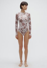 Long-sleeve floral swimsuit in brown and white. Features a fitted design with smooth texture and contrasting white side seams and accents.
