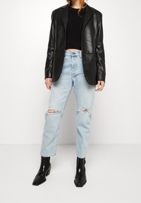 Schwarzer Lederblazer, kurz geschnitten, mit Reverskragen. Kombiniert mit hellblauen, verwaschenen Jeans. Schwarze Stiefeletten mit quadratischen Zehen.