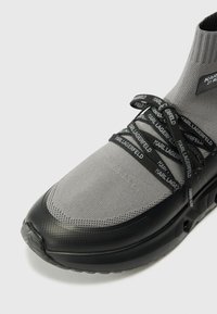 Gray sock-style sneaker with black accents; features textured upper, patterned laces, and smooth rubber sole with a carbon look.