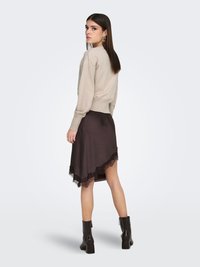 Pull beige en tricot à manches longues, associé à une jupe asymétrique marron avec un ourlet en dentelle. Bottines noires à finition texturée.
