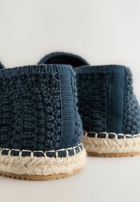 Zapatos slip-on de tela trenzada en azul marino con suelas de cuerda de yute, lados texturizados y un panel de tela reforzado en el talón.