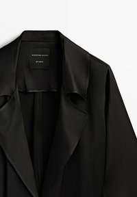 Czarny dopasowany płaszcz z szerokimi klapami, widocznym kołnierzem i metką "Massimo Dutti Studio" w okolicy szyi.