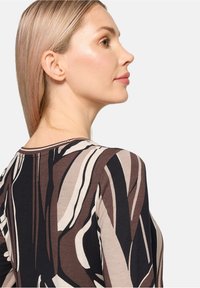 Dopasowana bluzka z długim rękawem w abstrakcyjnym wzorze w odcieniach brązu, czerni i kremu. Wykonana z miękkiego materiału, z okrągłym dekoltem i dopasowanym krojem.