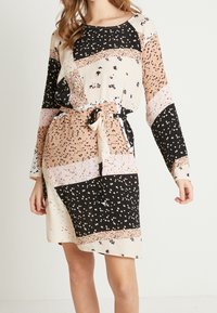Vestido de manga larga en un diseño de patchwork que presenta colores beige, negro y melocotón con patrones florales y una cintura ceñida con cinturón. Textura de tejido suave.