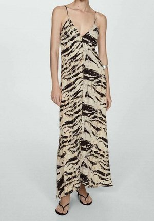 Frau trägt ein ärmelloses Maxi-Kleid in Beige und Schwarz mit Tigerstreifen, dünnen Trägern und schwarzen Sandalen mit offenen Zehen.