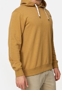 Sennepsgul hoodie med en kengurulomme, snor i hætten og ribbede manchetter. Lavet af blødt stof med en tekstureret overflade.