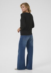 Maglione nero a coste con maniche a tre quarti abbinato a jeans blu a gamba larga. Il tessuto sembra morbido e ha una texture liscia.