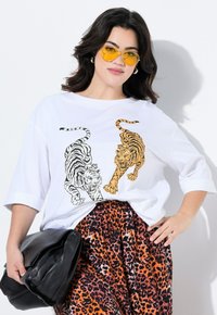 T-shirt oversize blanc avec des motifs de tigre noirs et orange. Associé à un pantalon à motifs léopard orange et noir, et un sac en cuir noir.