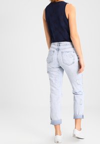 Marinblå ärmlös topp i kombination med slitna ljusblå jeans, uppvikta ärmslut och vita sneakers; har subtila fickdetaljer och blekt utseende.