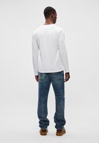 Langermet hvit bomullsskjorte med rund hals, kombinert med blå denimjeans. Jeansene har en falmet look og baklommer.