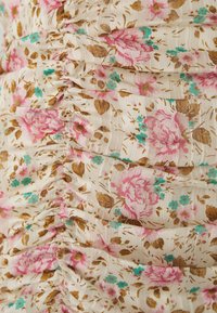 Tissu floral avec des roses roses et des accents turquoise sur un fond crème, présentant un design texturé et froncé tout au long.