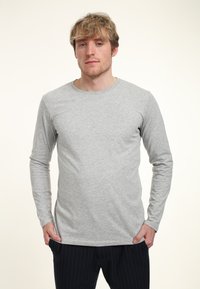 Šedé tričko s dlouhým rukávem vyrobené z bavlny, s kulatým výstřihem a úzkým střihem. Textura vypadá hladce s minimem švů.