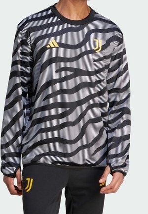 Personne porte un maillot à manches longues noir et blanc rayé zèbre avec des logos jaunes de la Juventus et Adidas, associé à un pantalon noir.