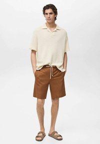 Krémovo textúrované polo tričko s krátkym rukávom v kombinácii s hnedými šortkami so sťahovacou šnúrkou. Sandále dopĺňajú outfit a zdôrazňujú letný ležérny štýl.