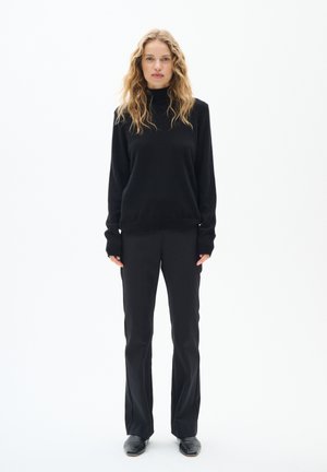 Black turtleneck sweater with long sleeves, paired with black tailored trousers and black shoes, set against a plain white background.