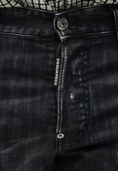 Κοντινό πλάνο σε μαύρα ξεθωριασμένα τζιν με μερικώς ανοιχτό φερμουάρ και ετικέτα "DSQUARED2" στο εμπρός μέρος κάτω από ένα μεταλλικό κουμπί.