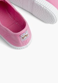 Botte en toile rose avec une semelle en caoutchouc blanche, ornée d'un bord surpiqué et d'une petite étiquette avec un design de singe sur le côté.