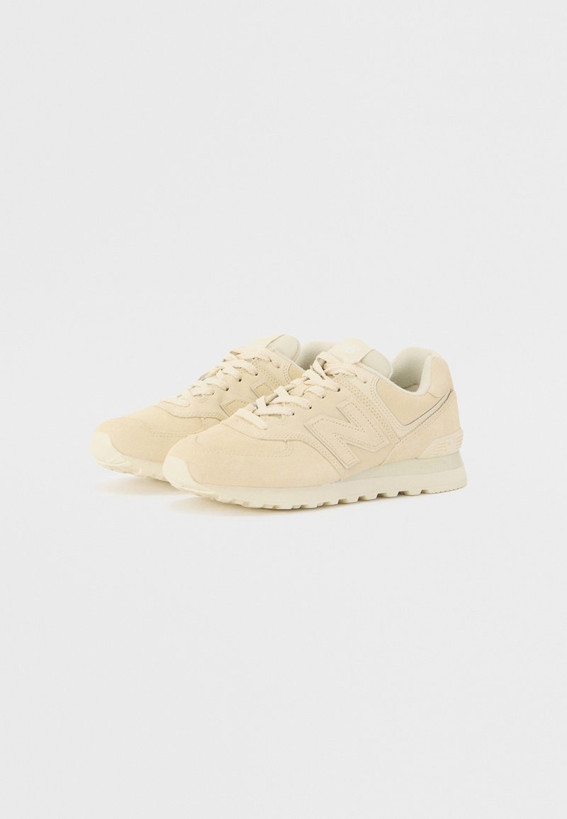 Zapatillas deportivas beige con parte superior de ante, acentos texturizados, cierre de cordones y suela acolchada. Presenta un gran logo "N" en el lateral.