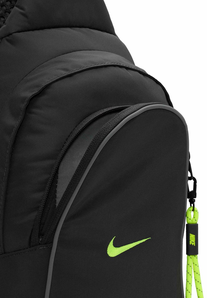 Czarny plecak nylonowy z wyraźnym zielonym logo Nike, gładką teksturą oraz zamykaną na zamek kieszenią z kontrastowym szarym obwodem.