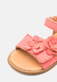 Rosa lærsandaler med blomsterelementer, åpen tå, justerbar stropp med sølvdetaljer og en brun flat såle.