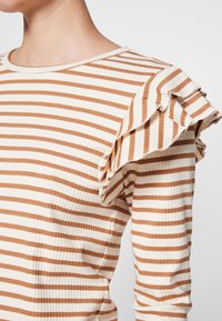 Gestreiftes Oberteil in Beige und Braun, mit gerippter Textur, rundem Ausschnitt und Rüschendetails an den Ärmeln.