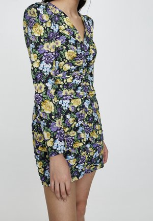 Robe mini florale à manches longues ; présente un fond noir, des roses jaunes et violettes, ainsi que des fleurs bleues ; texture froncée sur les côtés.