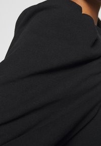 Black cotton fabric with a ribbed texture, featuring draped folds and a smooth finish. Design emphasizes comfort and relaxed fit.