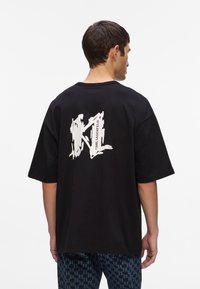Zwarte oversized t-shirt van katoen, met een groot wit grafisch ontwerp op de achterkant, met daaronder de tekst "Karl Lagerfeld".
