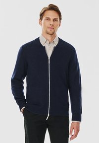 Navy rozpinany kardigan wykonany z miękkiego materiału, z okrągłym dekoltem, prążkowanymi mankietami i srebrnym zamkiem błyskawicznym. Noszony na lekką koszulę.