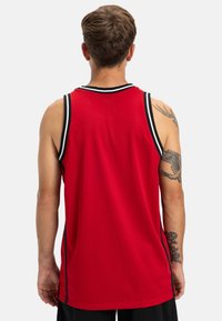 Červený športový dres s sieťovinovou textúrou, čiernymi akcentovými pruhmi, bez rukávov a okrúhlym výstrihom, s hladkým chrbtom.