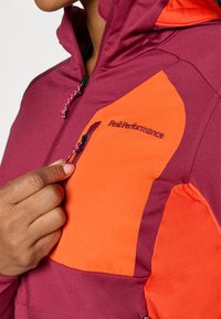Paarse en oranje jas met een ritszak, voorzien van een verstelbaar koord, gemaakt van een gladde, duurzame stof met tonale stiksels.