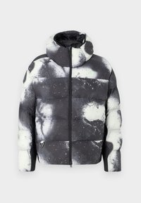 Jachetă pufoasă alb-negru cu un model abstract de stropi, închidere cu fermoar și guler înalt. Prezintă un logo triunghiular distinctiv.