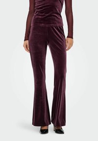 Vinrøde fløjlsbukser med flare og blød tekstur, med elastisk taljebånd og tætsiddende silhuet, kombineret med en matchende top.