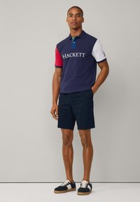 Polo en navy, blanco y rojo con logo de "HACKETT"; material de algodón. Combinado con pantalones cortos navy y zapatillas navy con detalles en blanco.