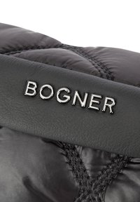 Svart quiltad puffermaterial med en strukturerad läderremsa där det präglade varumärkesnamnet "BOGNER" framträder i glänsande silverbokstäver.