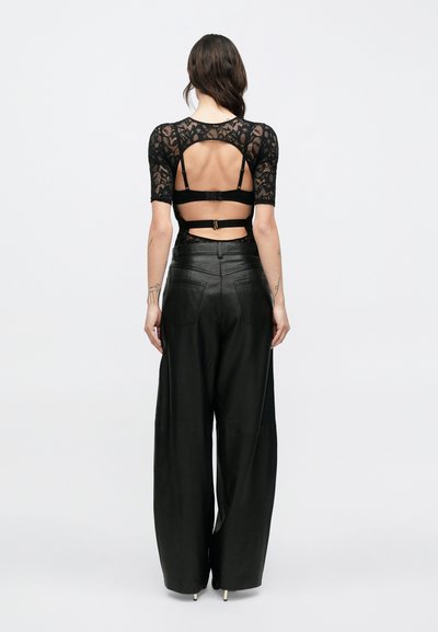 Fekete csipkefelső rövid ujjakkal, hátul kivágással és állítható pántokkal. Magas derekú, széles szárú fekete bőr nadrággal párosítva.