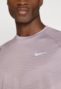 Αθλητικό μπλουζάκι σε ανοιχτό μωβ χρώμα με στρογγυλή λαιμόκοψη, αναπνεύσιμο υλικό κα�ι μικρό λευκό λογότυπο Nike στην αριστερή πλευρά του στήθους.